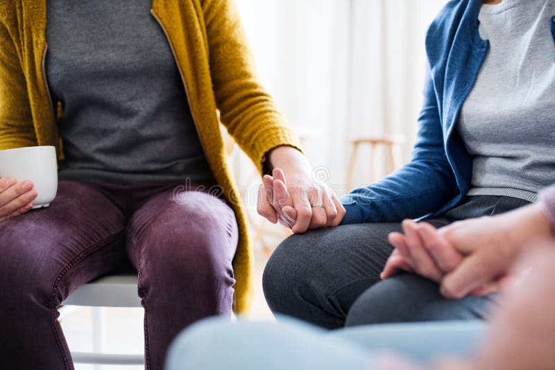 Midsection of men and women sitting in a circle during group therapy, supporting each other and holding hands. Midsection of men and women sitting in a circle during group therapy, supporting each other and holding hands.